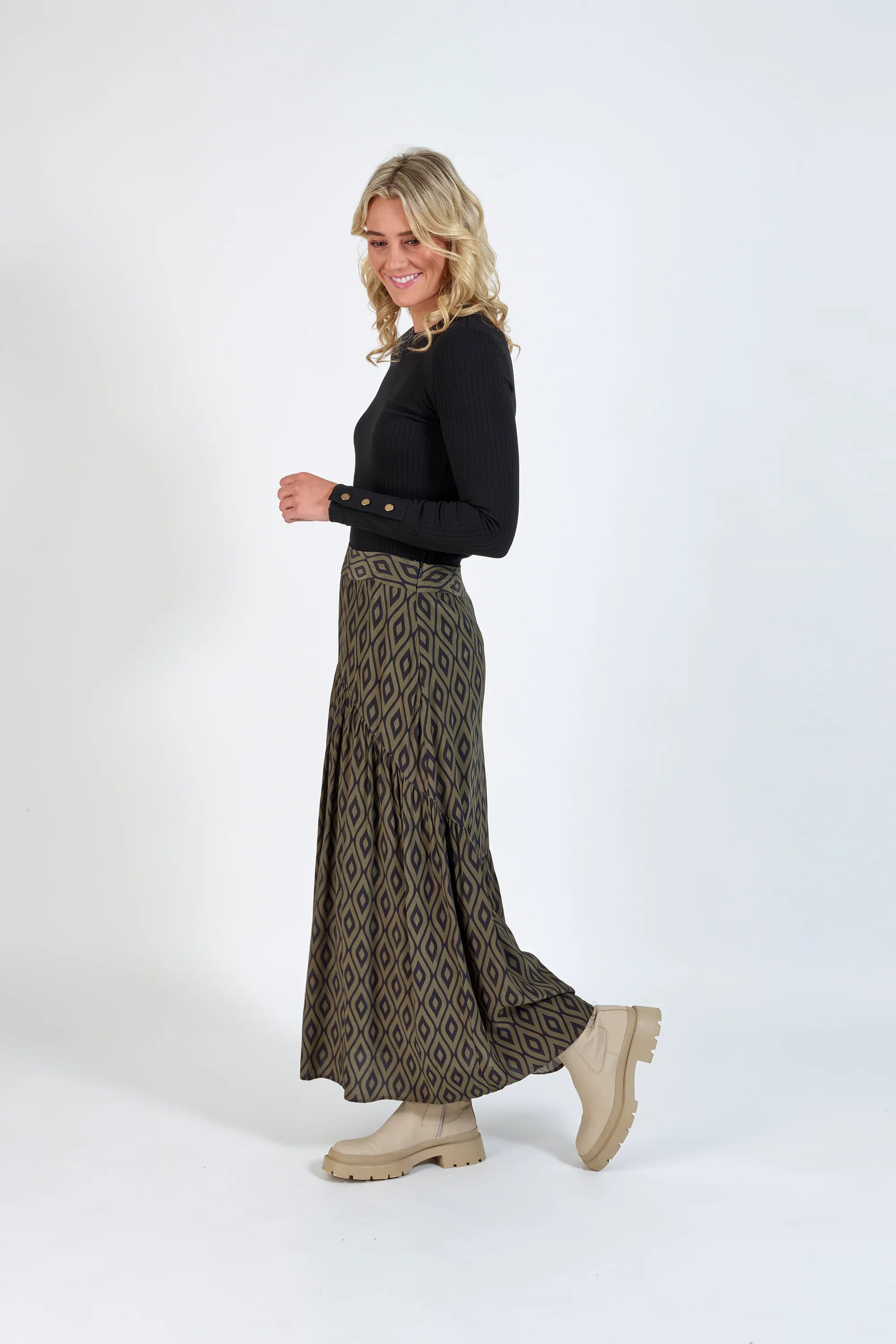 Woman wearing a black long sleeve top, geometric print maxi skirt, and beige boots