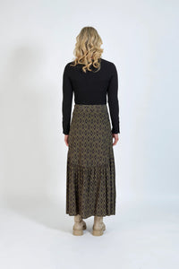 Back view of woman wearing long geometric patterned skirt, black top, and beige boots
