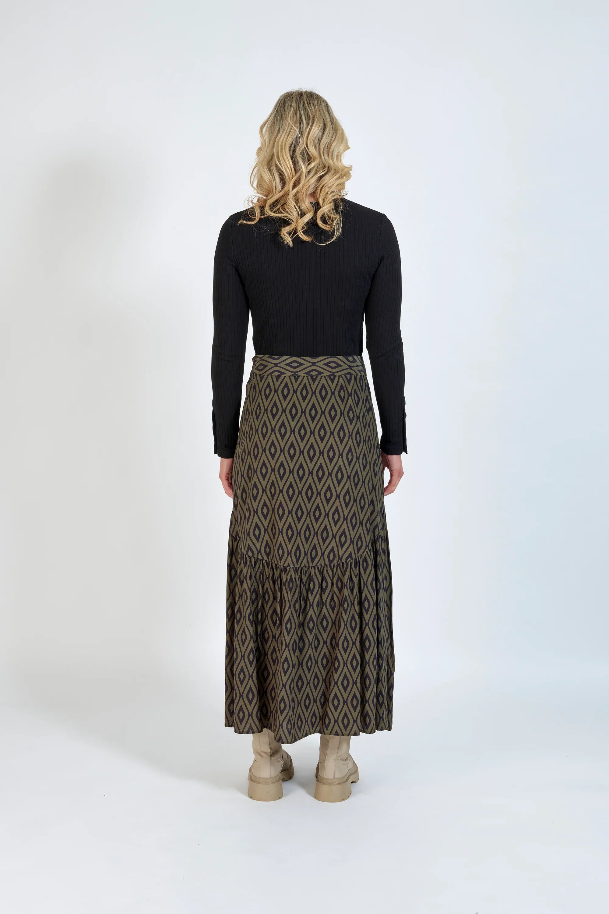 Back view of woman wearing long geometric patterned skirt, black top, and beige boots
