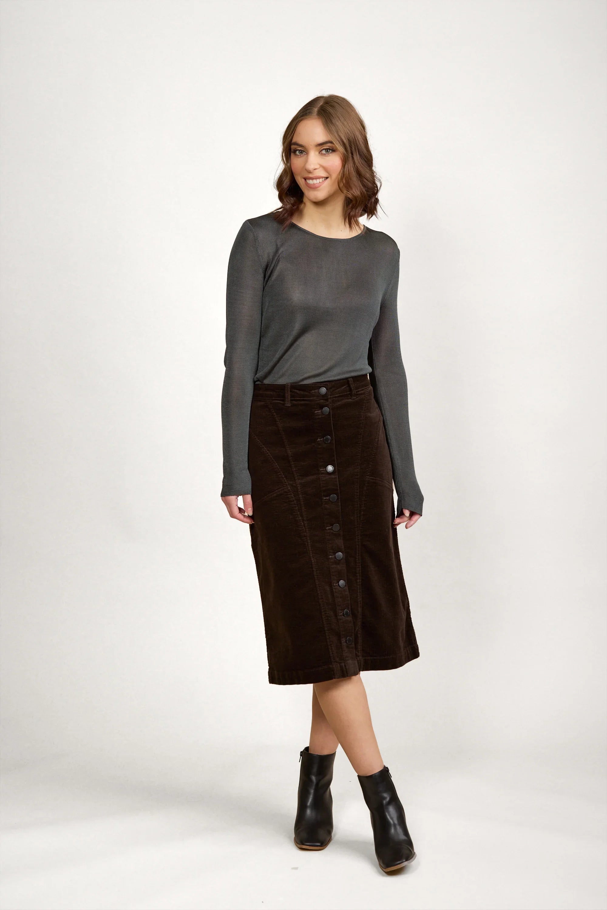 Woman wearing a charcoal long sleeve top and dark brown corduroy button-front midi skirt