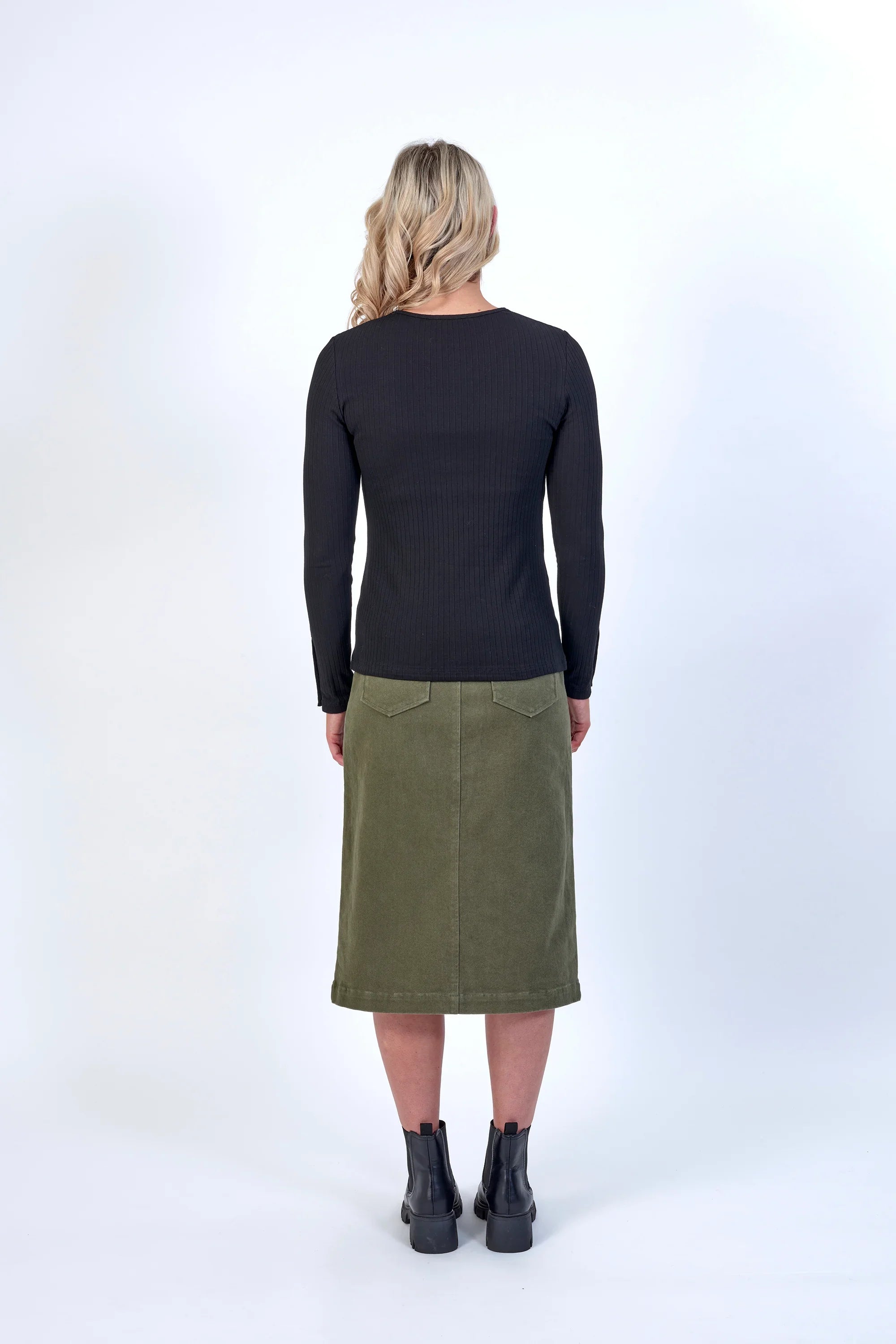 Back view of woman in a khaki midi skirt, black ribbed top, and ankle boots
