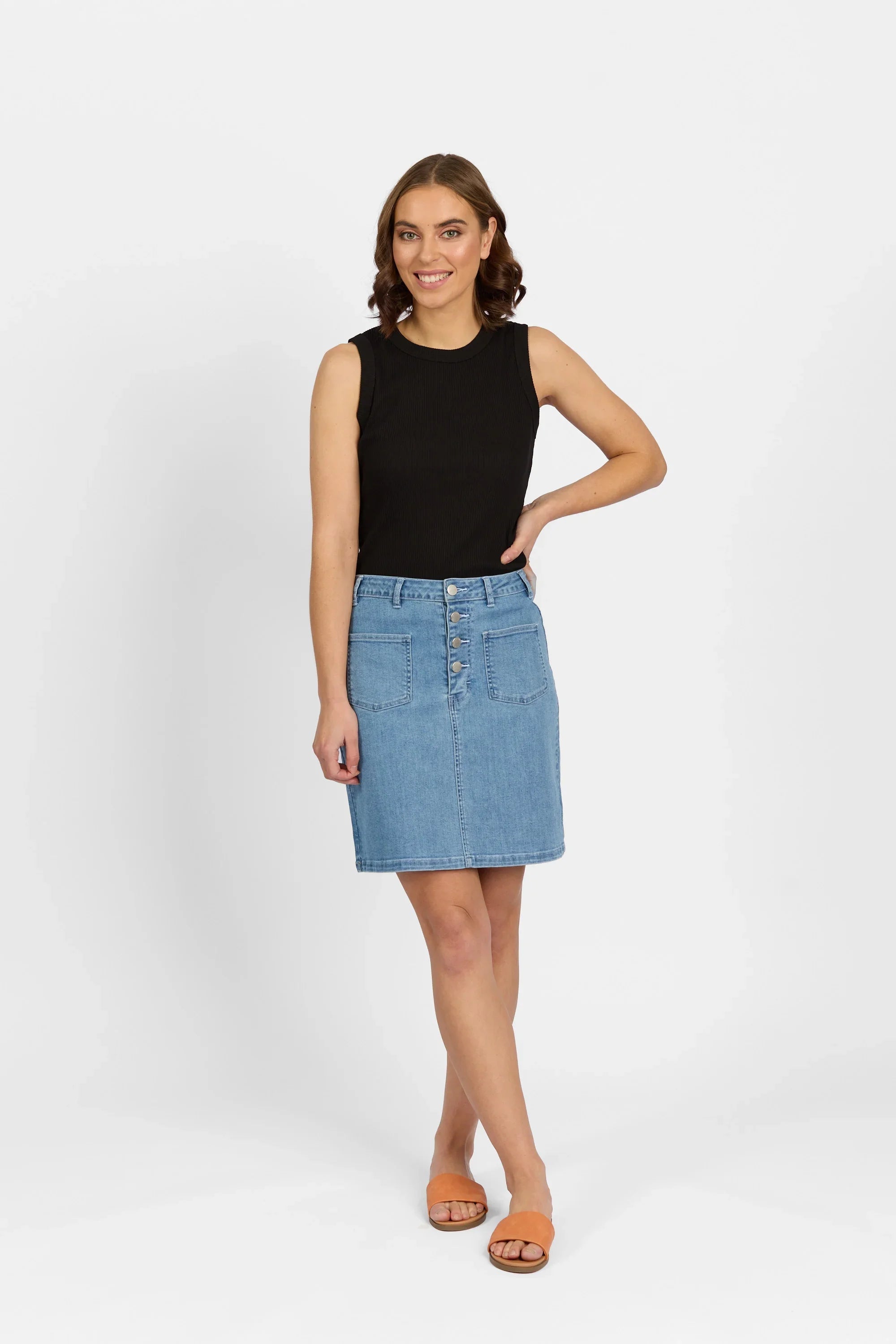 Woman in a sleeveless black top and light blue denim skirt with front buttons and pockets.