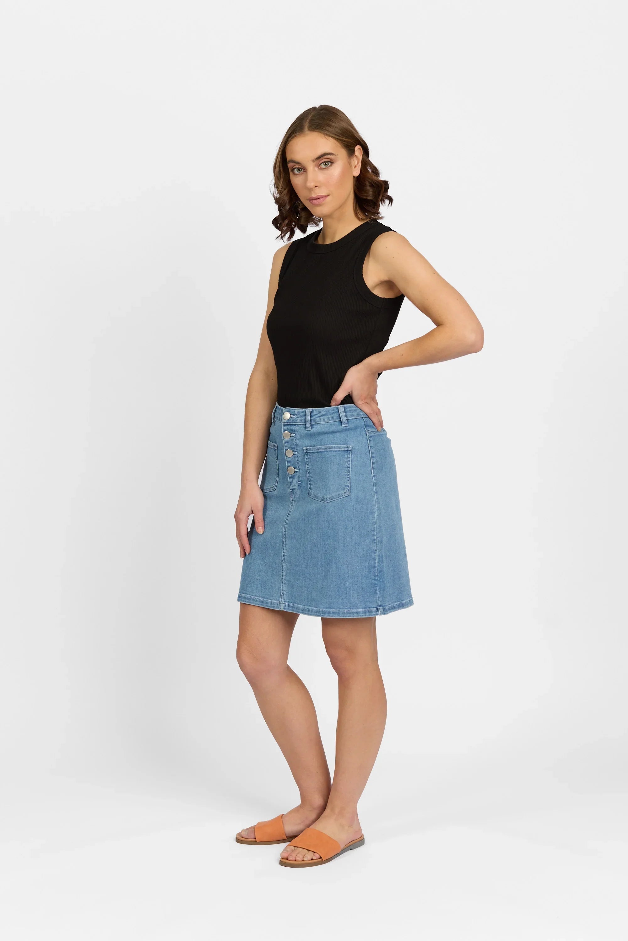 Woman wearing a blue button-front denim skirt, black sleeveless top, and orange sandals
