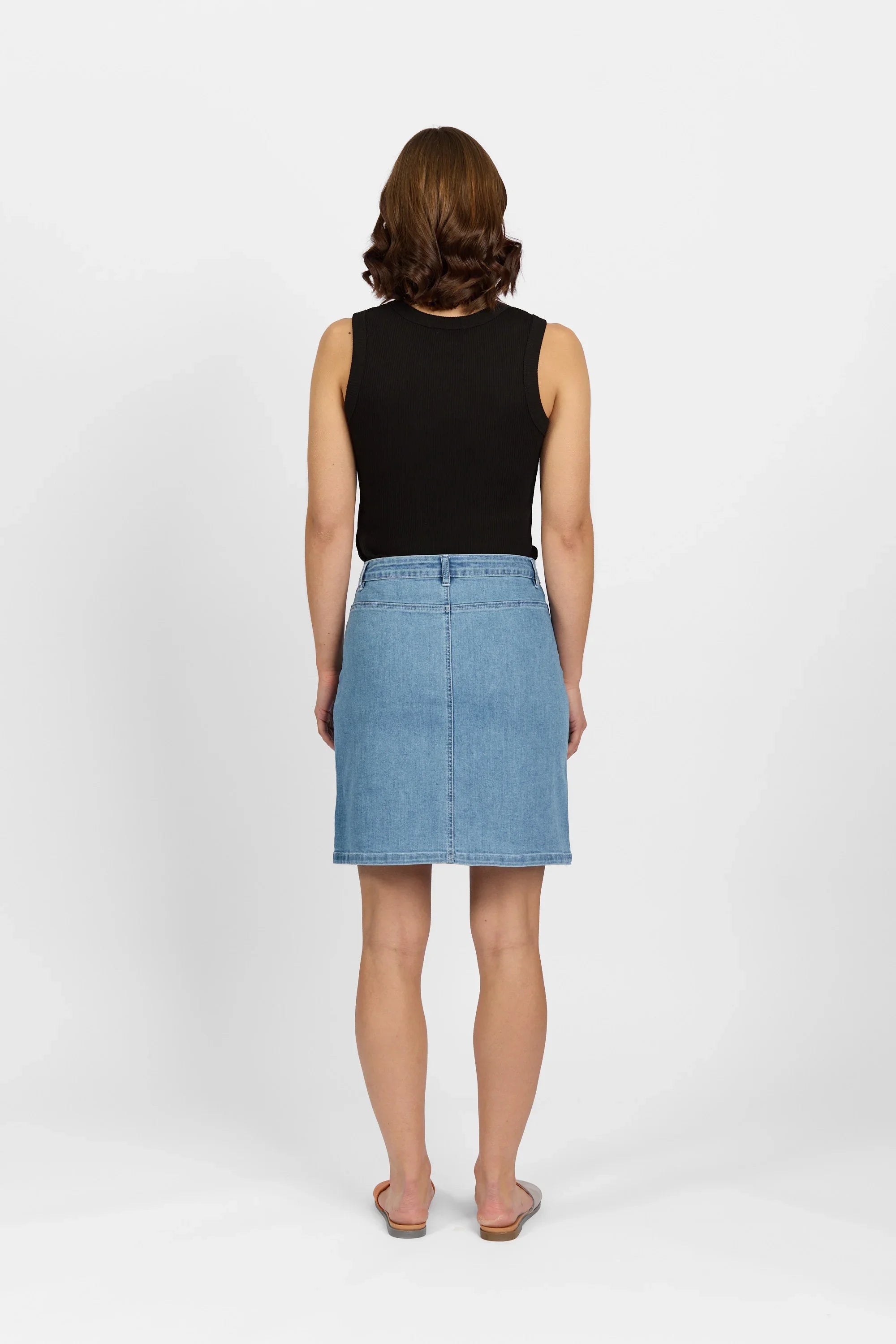 Woman wearing a light blue denim skirt and black sleeveless top, back view, studio setting