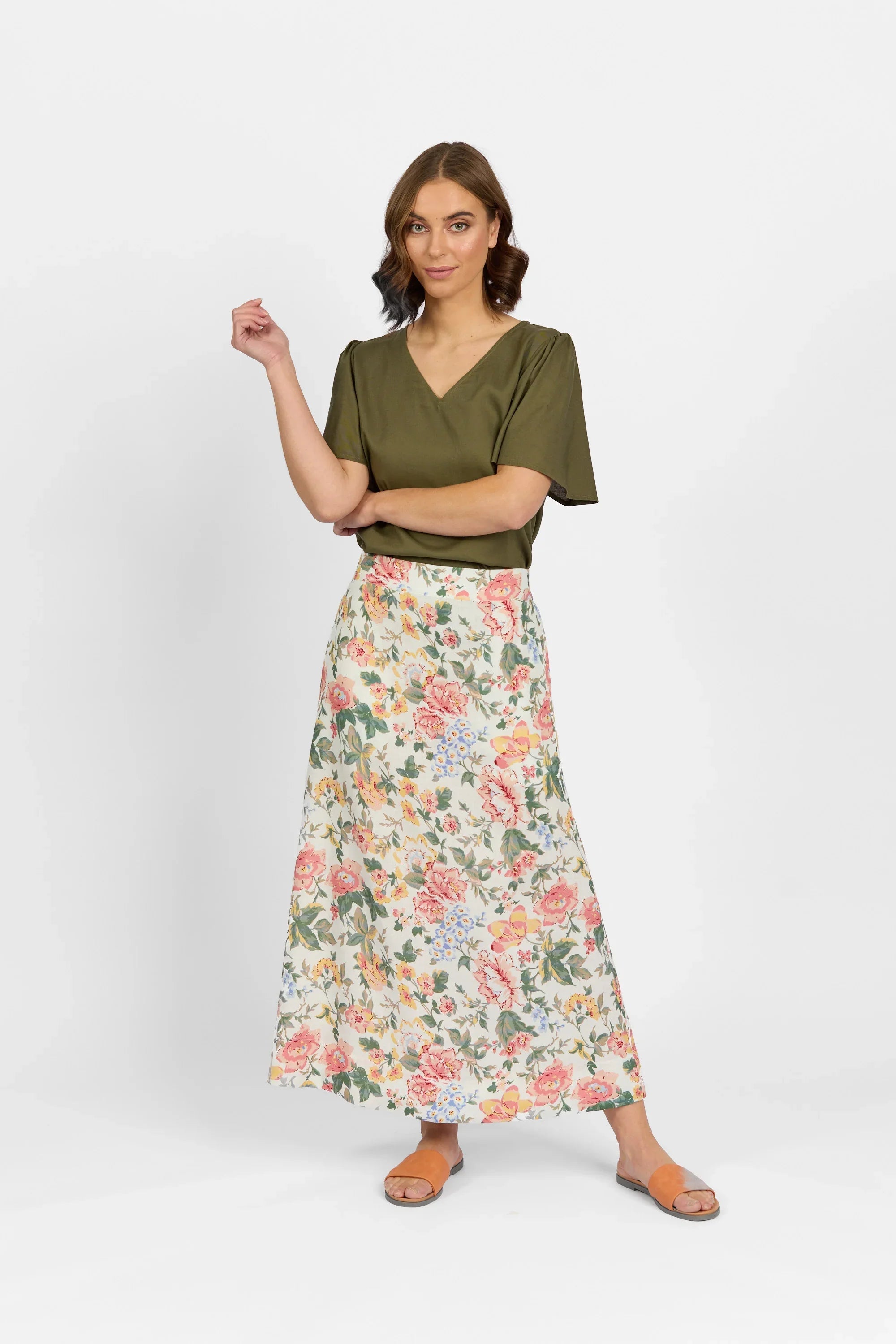 Woman in olive green top and floral print maxi skirt, standing against white background
