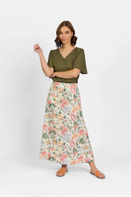 Woman in olive green top and floral print maxi skirt, standing against white background
