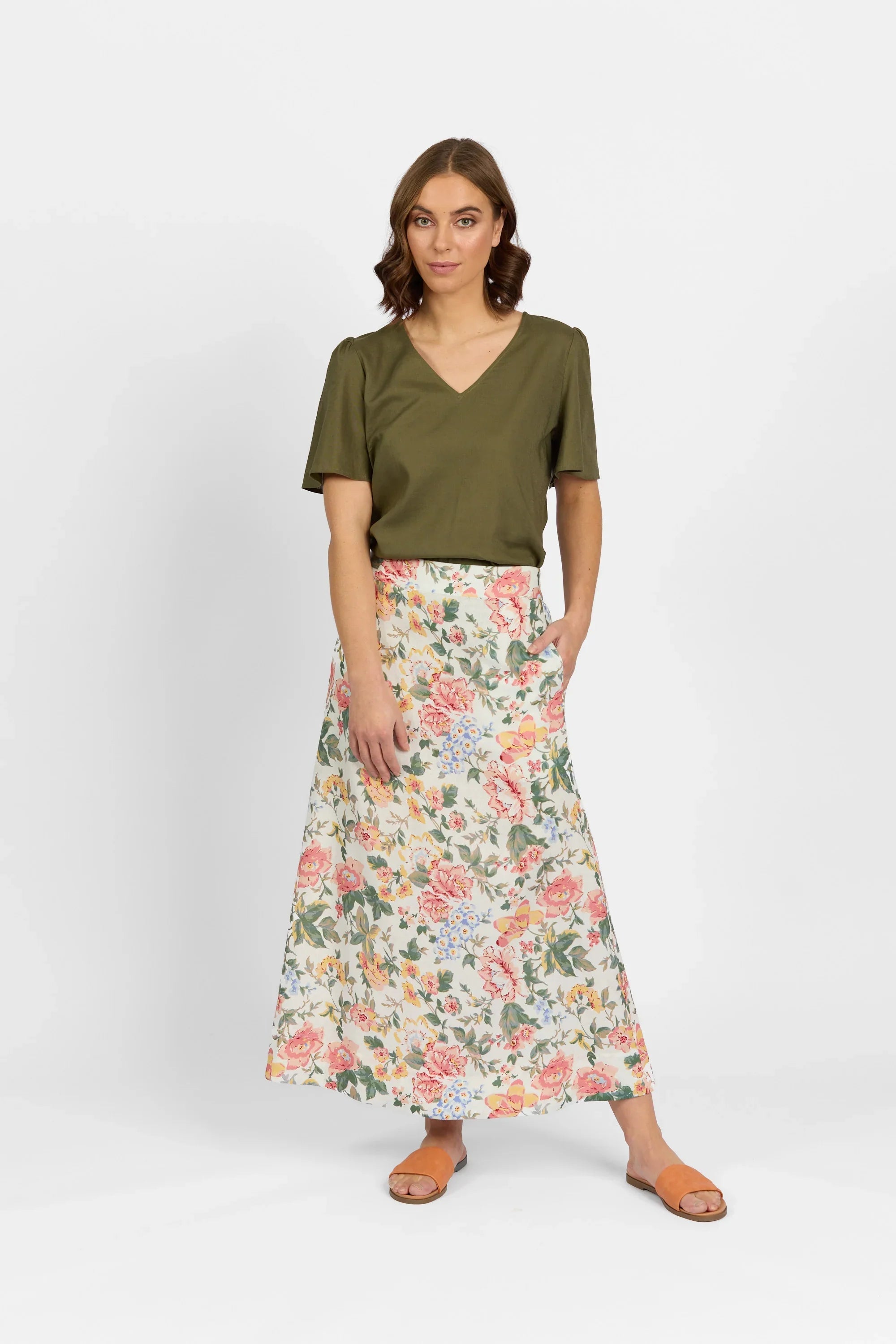 Woman wearing khaki V-neck top and floral print maxi skirt, standing against white background
