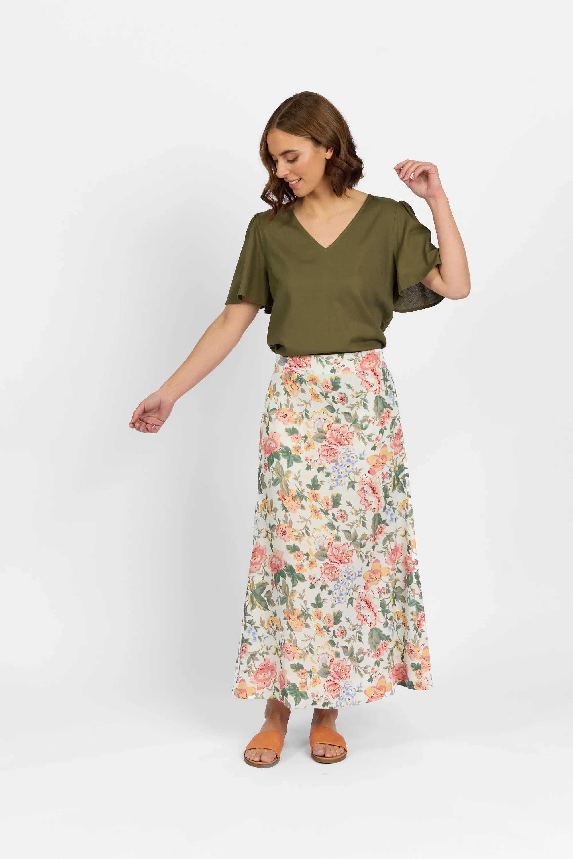 Woman wearing olive green v-neck blouse and long floral print skirt, standing indoors