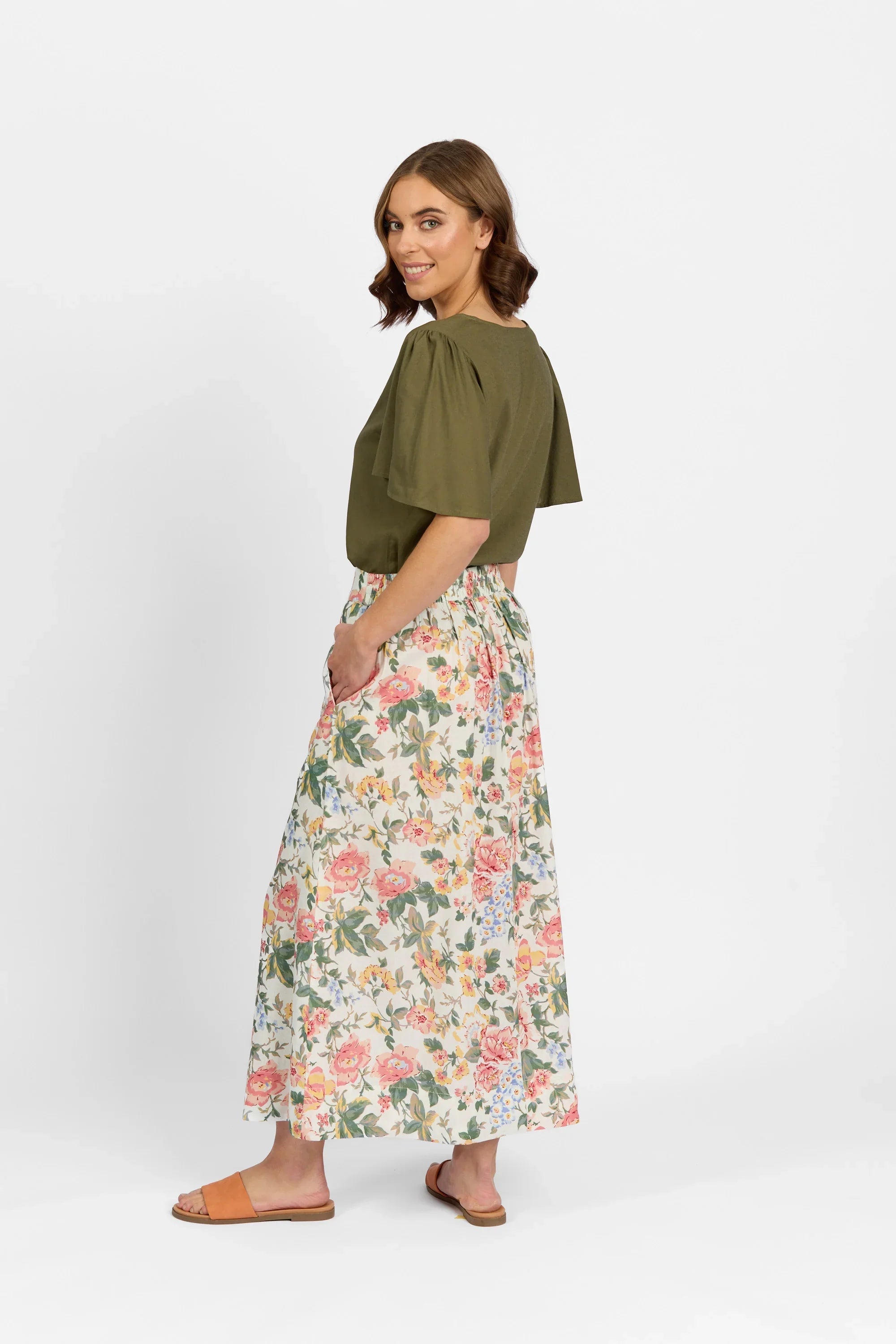 Woman in olive green blouse and floral maxi skirt with pockets, side view, white background