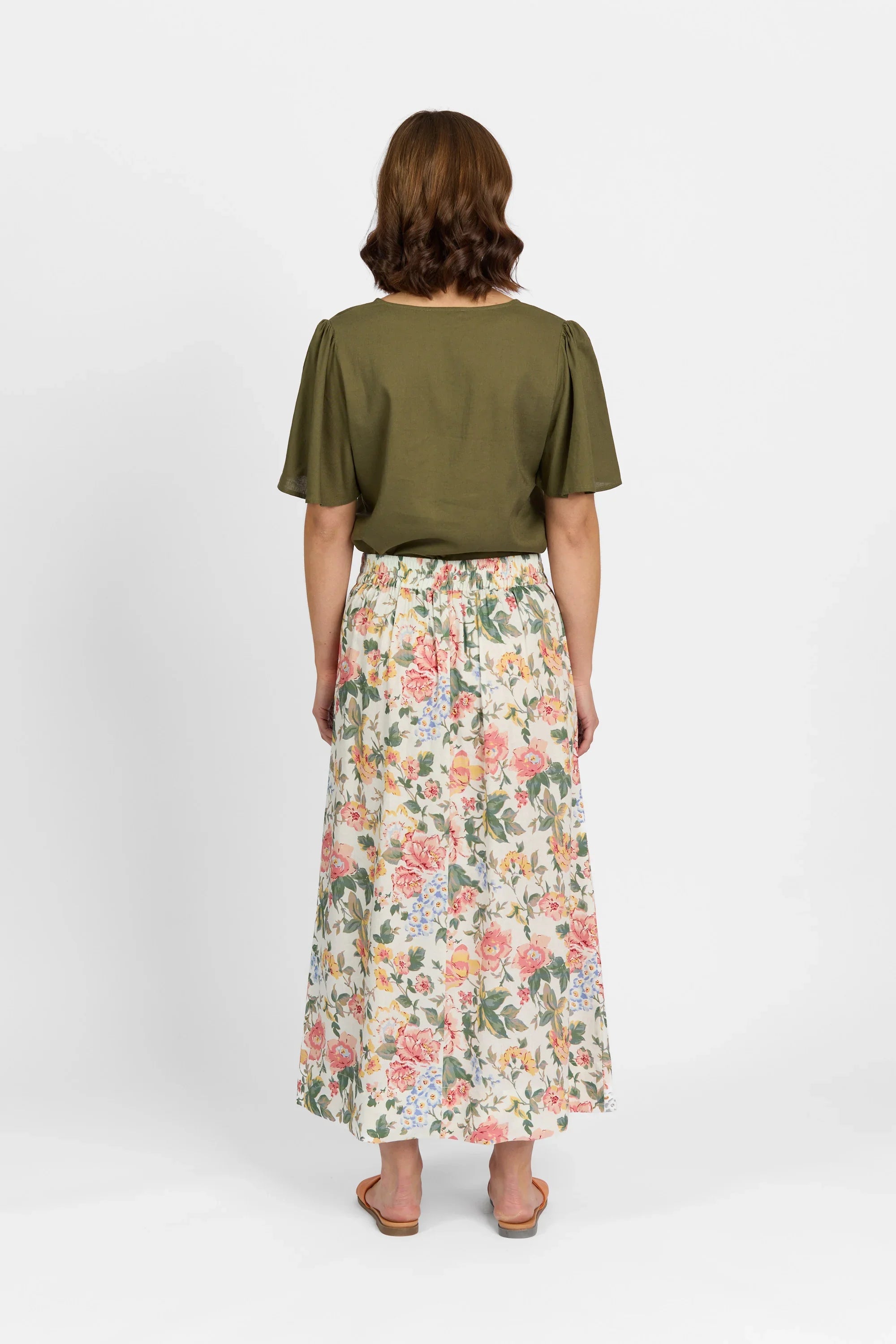 Woman in olive green blouse and floral print maxi skirt standing against white background