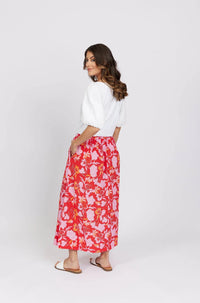Woman in a white blouse and red floral maxi skirt with pockets, standing in profile