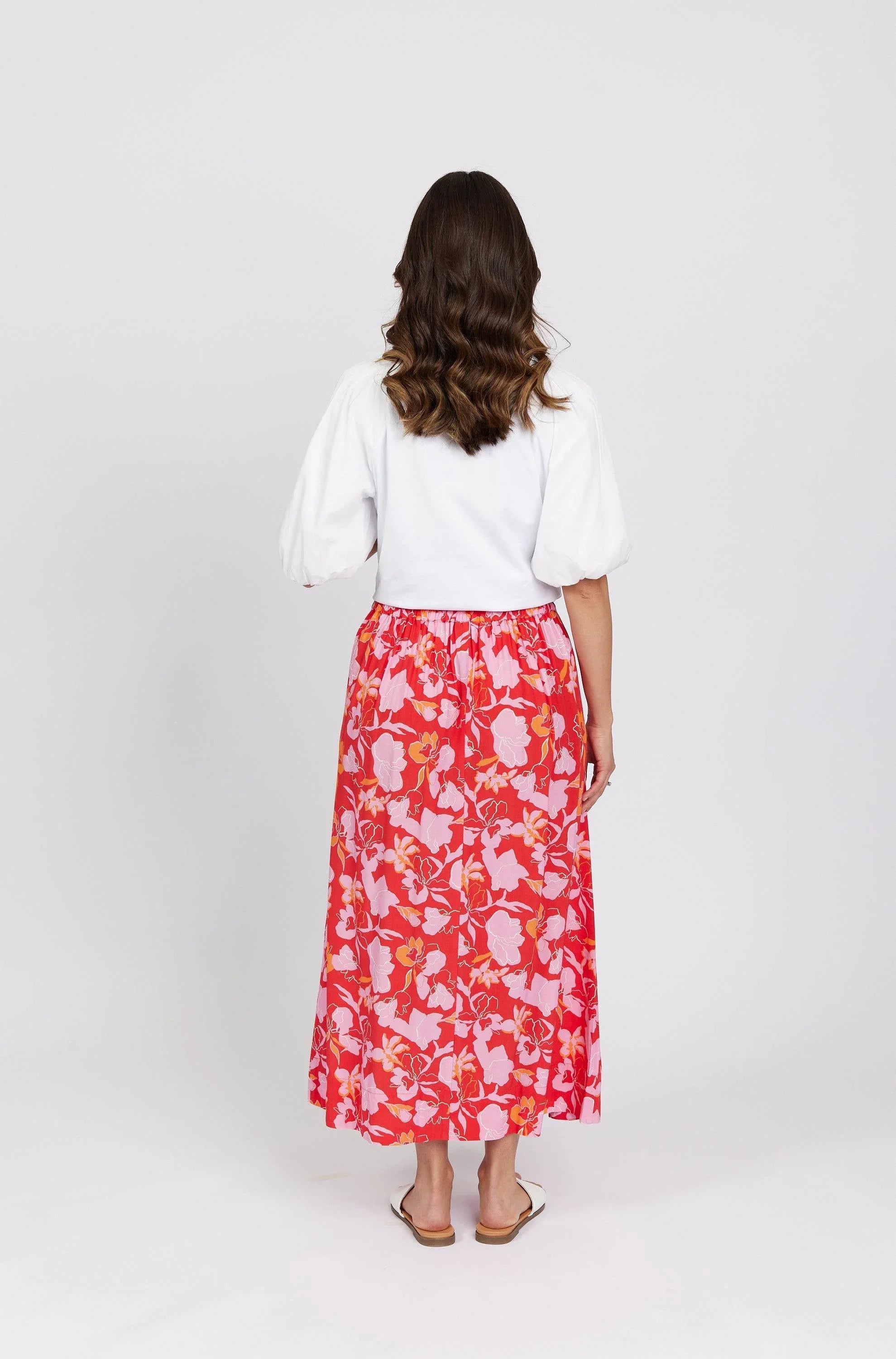 Woman in white puff sleeve top and red floral midi skirt, standing on white background