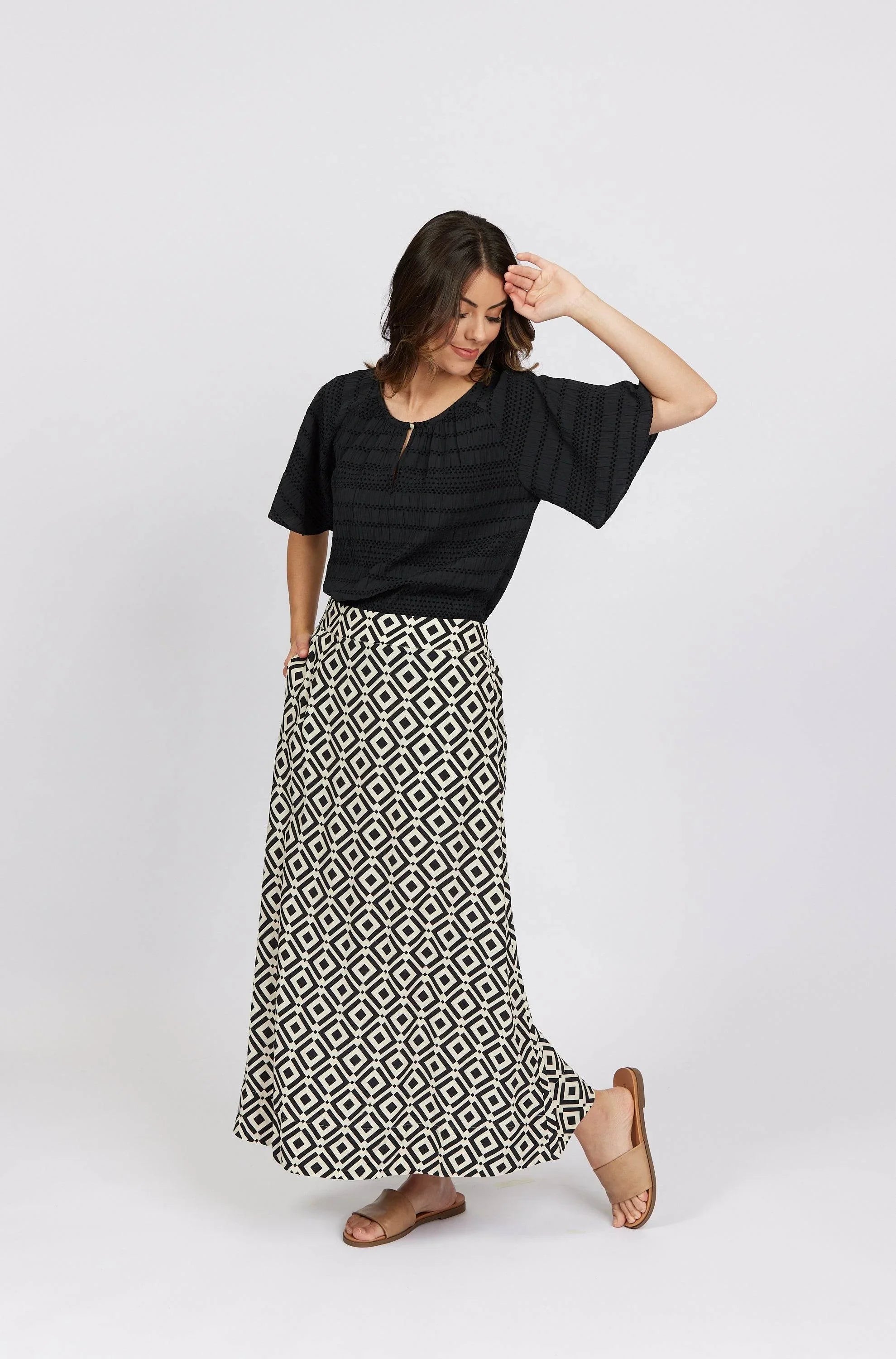 Woman wearing black blouse with geometric print maxi skirt and tan sandals