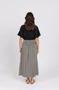 Woman wearing black top and geometric print maxi skirt, back view, studio setting