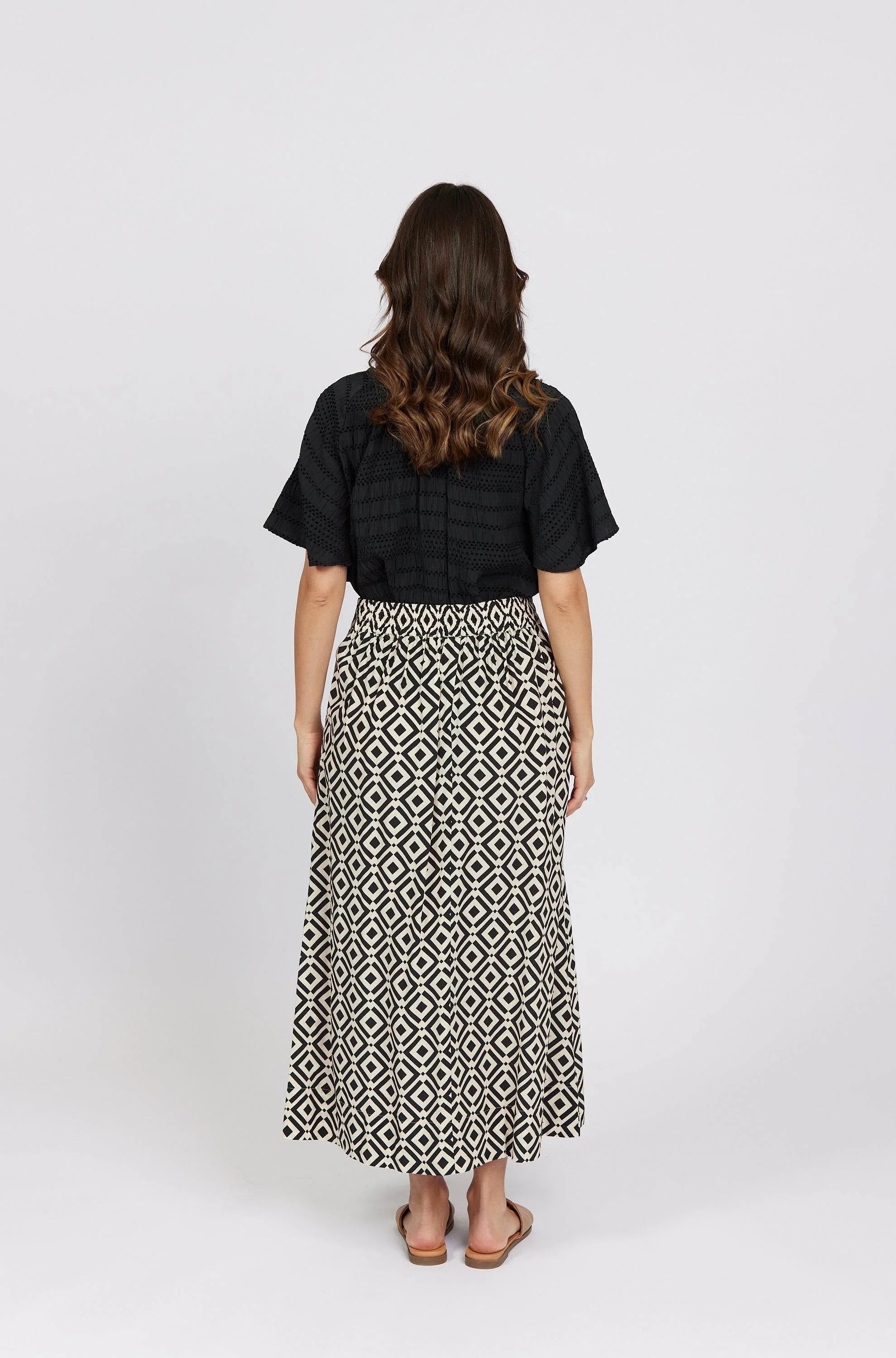 Woman wearing black top and geometric print maxi skirt, back view, studio setting