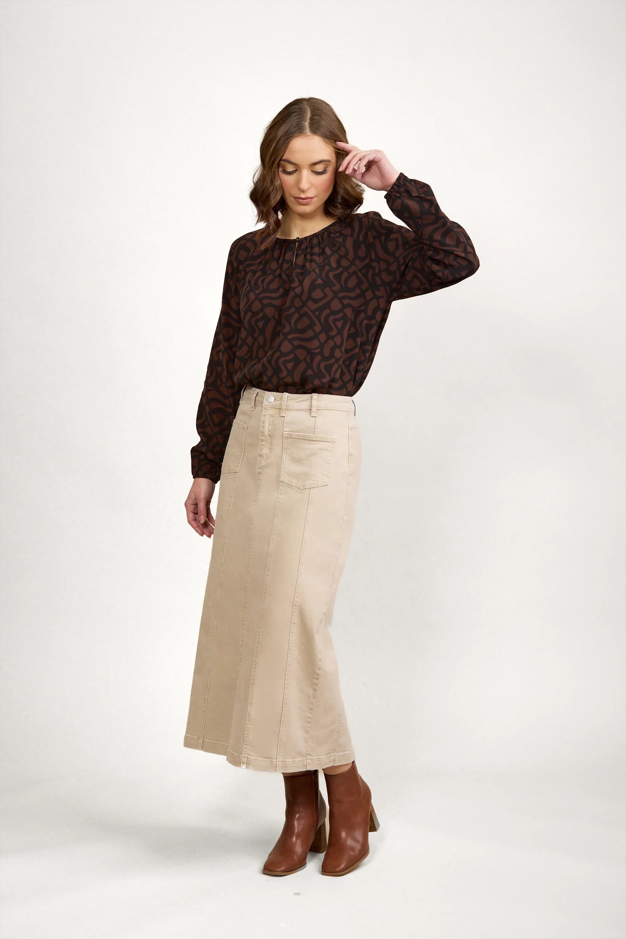 Woman wearing oat denim midi skirt with front seam, brown patterned blouse, and tan boots