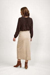 Woman wearing an oat denim midi skirt, brown abstract blouse, and ankle boots, back view.