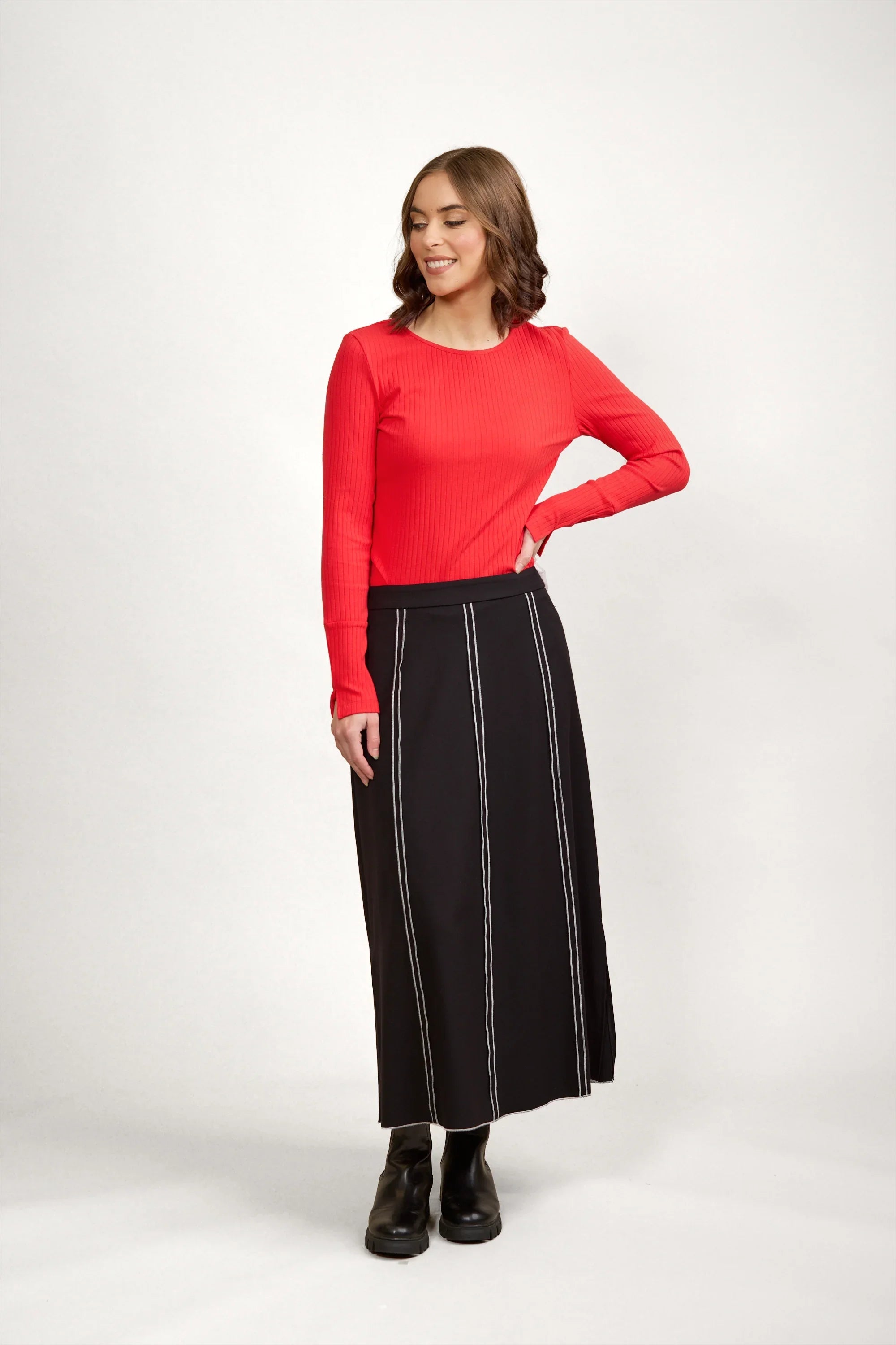 Woman in long black skirt with white vertical stitching, red ribbed top, and black boots