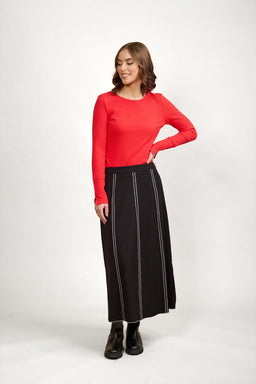 Woman in long black skirt with white vertical stitching, red ribbed top, and black boots