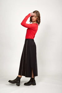 Woman in black midi skirt with white stitching, red long sleeve top, and black ankle boots