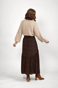 Woman wearing mocha patterned maxi skirt with beige knit sweater and brown boots, back view