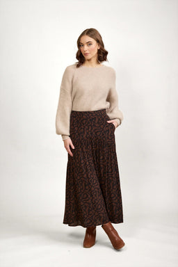 Woman wearing a mocha brown patterned maxi skirt, beige knit sweater, and brown boots