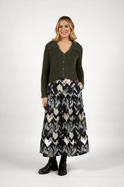 Woman wearing a green knit cardigan and black-white patterned maxi skirt with boots.