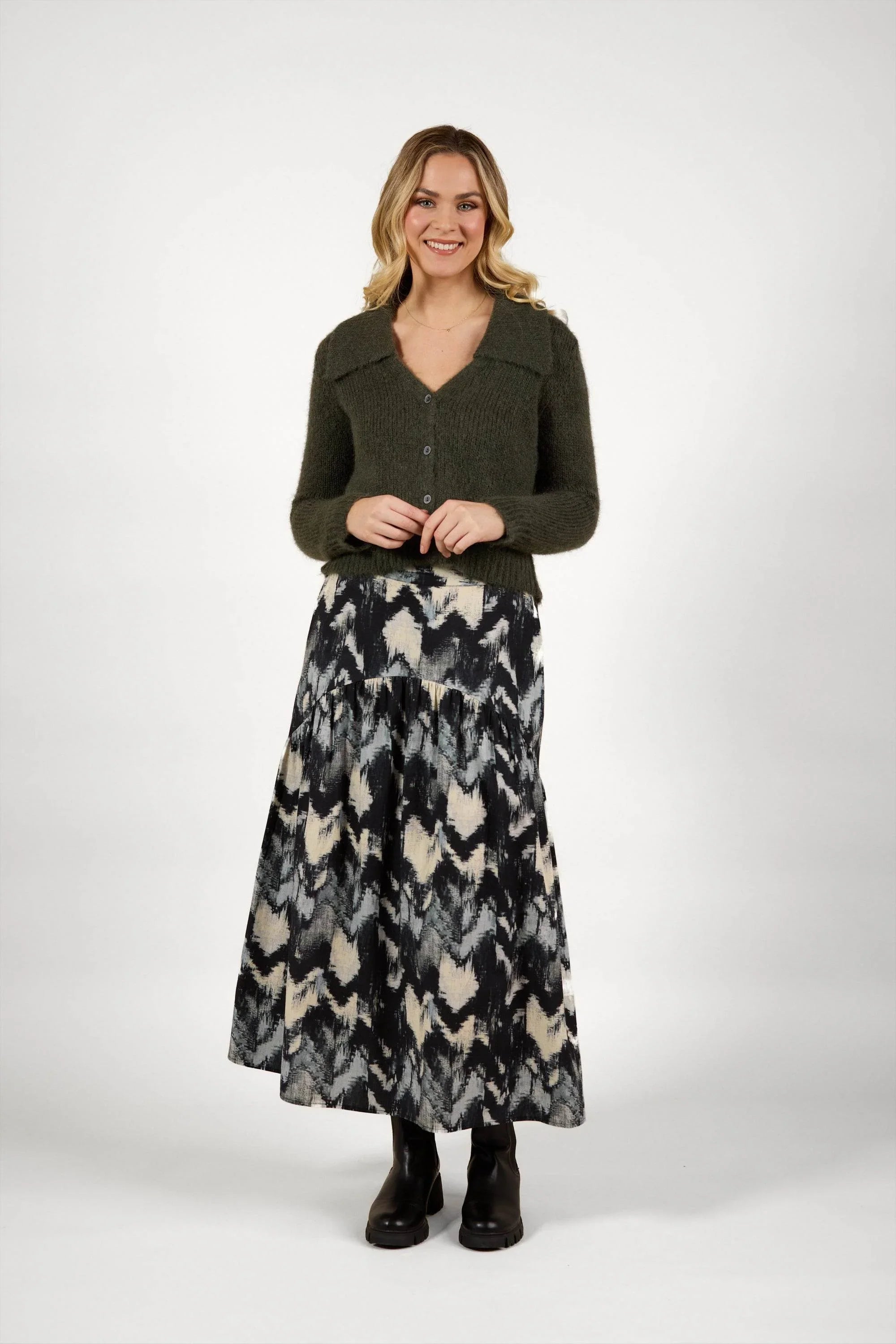 Woman wearing olive buttoned knit sweater and black abstract print maxi skirt with boots