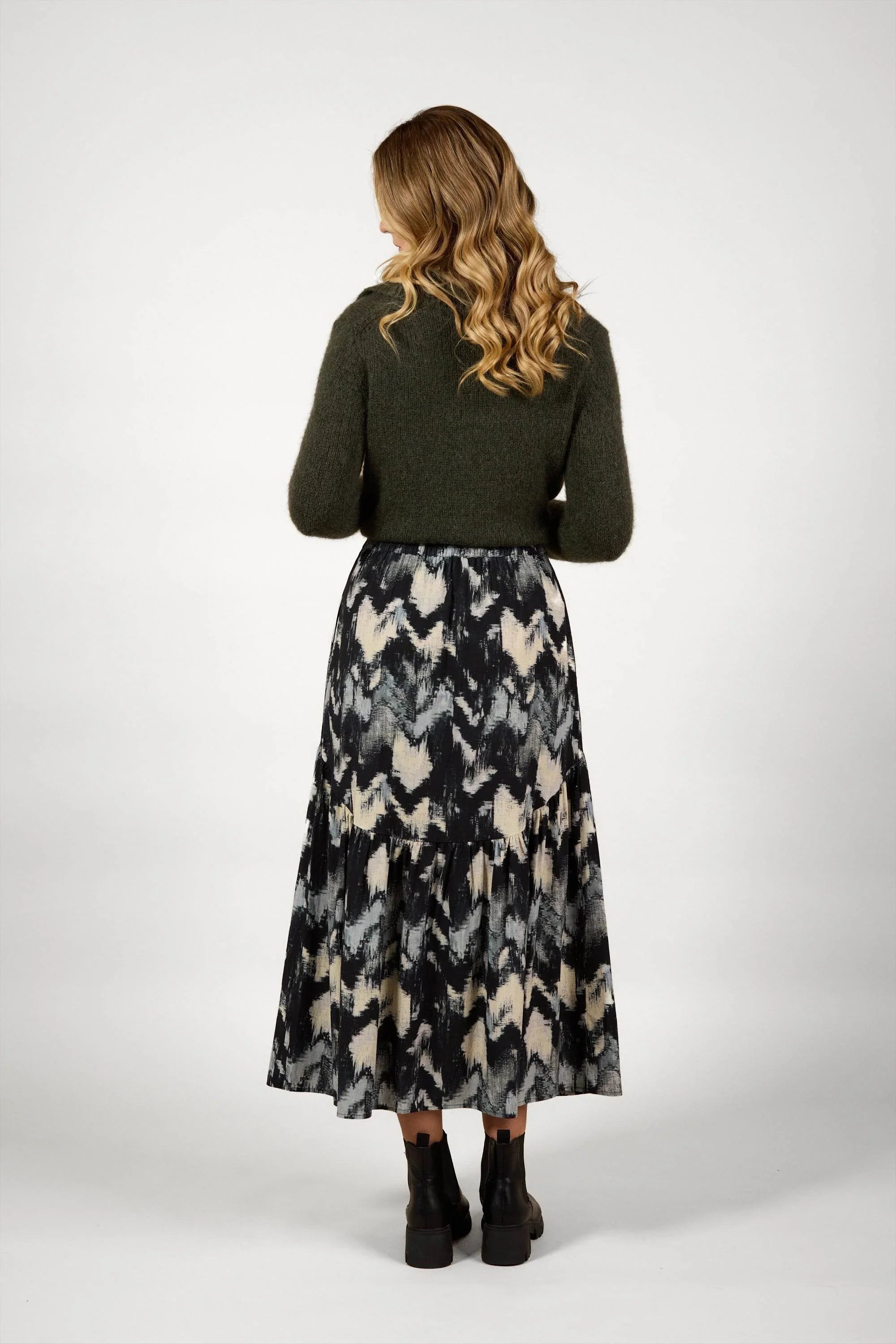 Woman in dark green sweater and abstract print midi skirt, rear view, fashion studio shot