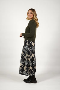 Woman in olive knit sweater and abstract print maxi skirt with black boots standing sideways