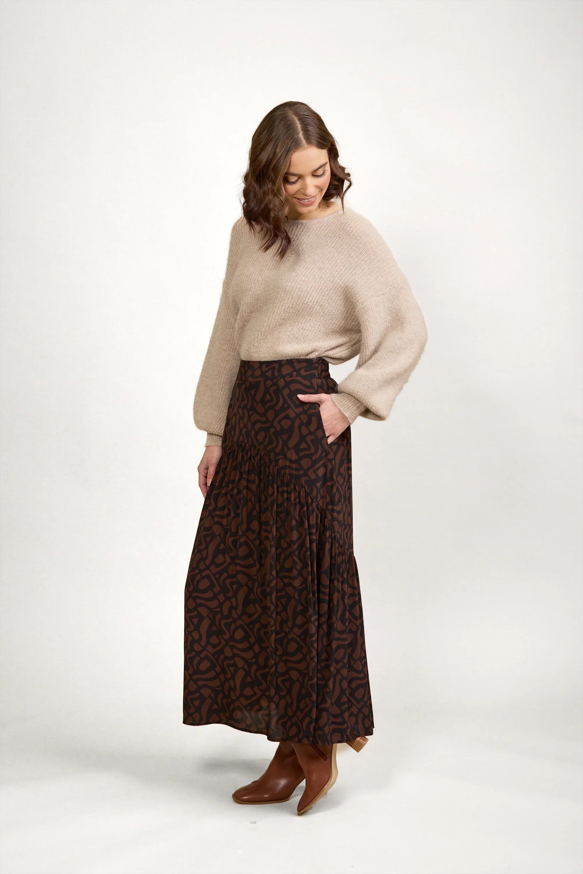 Woman wearing a beige knit sweater and a brown patterned maxi skirt with boots