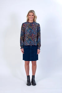 Woman wearing long sleeve colorful print blouse, navy skirt, and black ankle boots