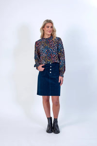 Woman in colorful print long sleeve blouse and dark blue skirt, black ankle boots, studio background