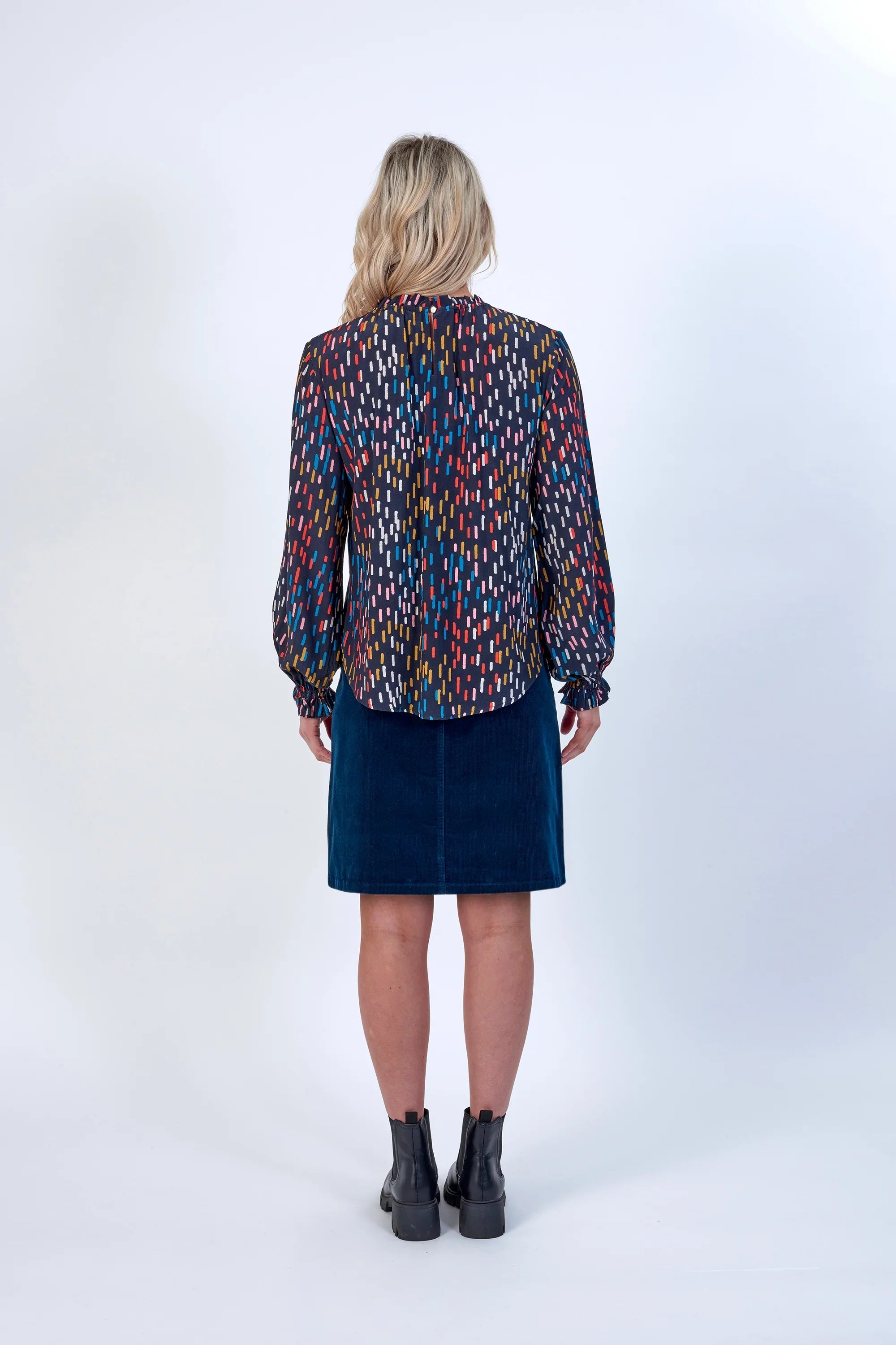 Woman in multicolored long-sleeve blouse and blue skirt, viewed from the back