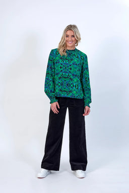 Woman wearing green geometric patterned long-sleeve blouse and black wide-leg pants