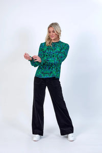 Woman wearing a long-sleeve green geometric print top with black wide-leg pants and white sneakers