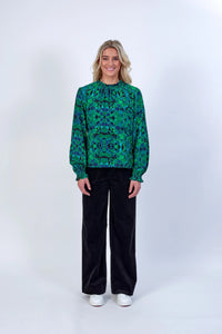 Woman wearing a green geometric print long sleeve blouse with black wide-leg pants