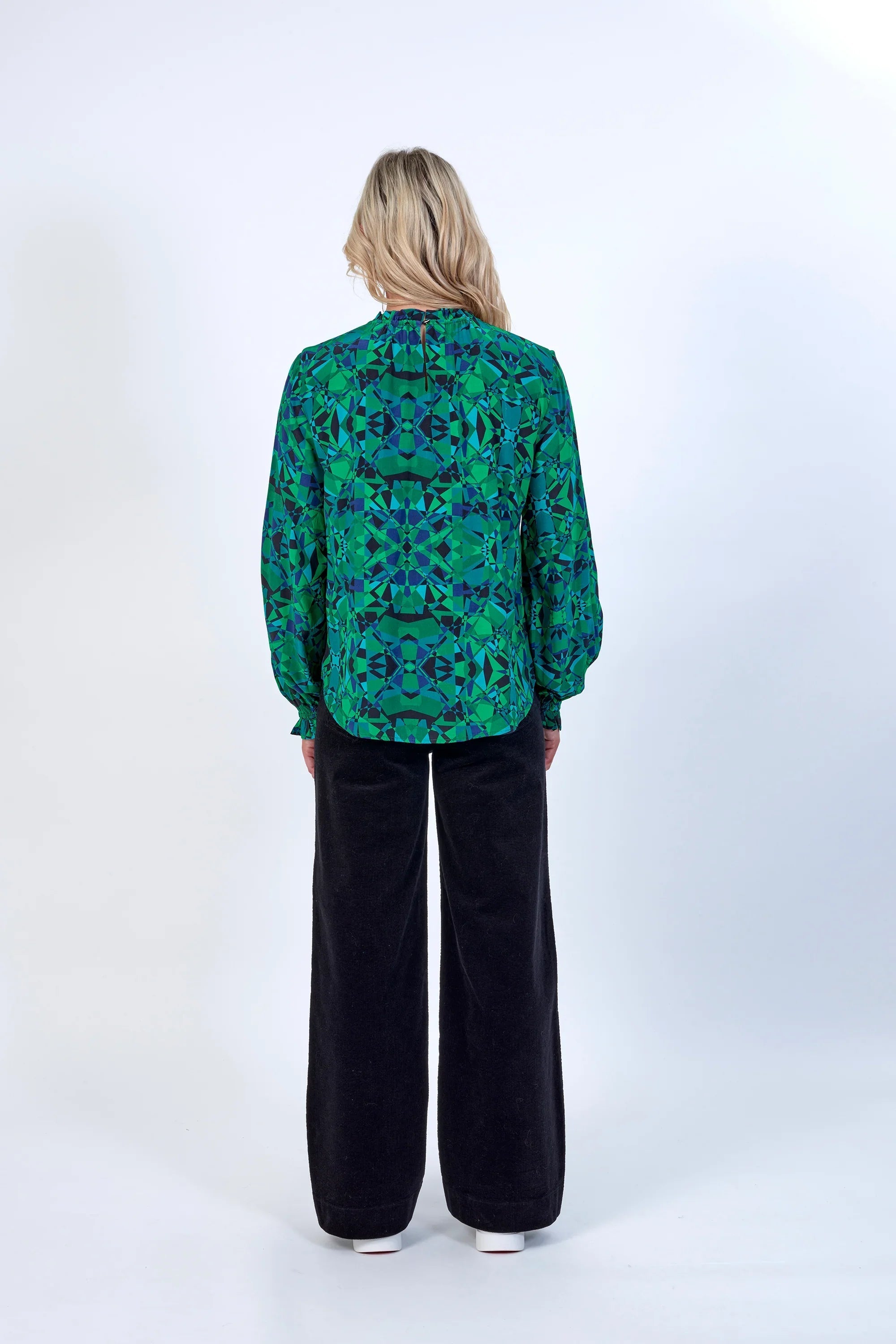 Back view of woman in green geometric print blouse with long sleeves and black wide-leg pants