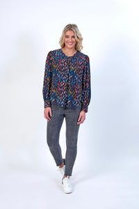 Woman wearing a long sleeve multicolor patterned top with grey skinny jeans and white sneakers