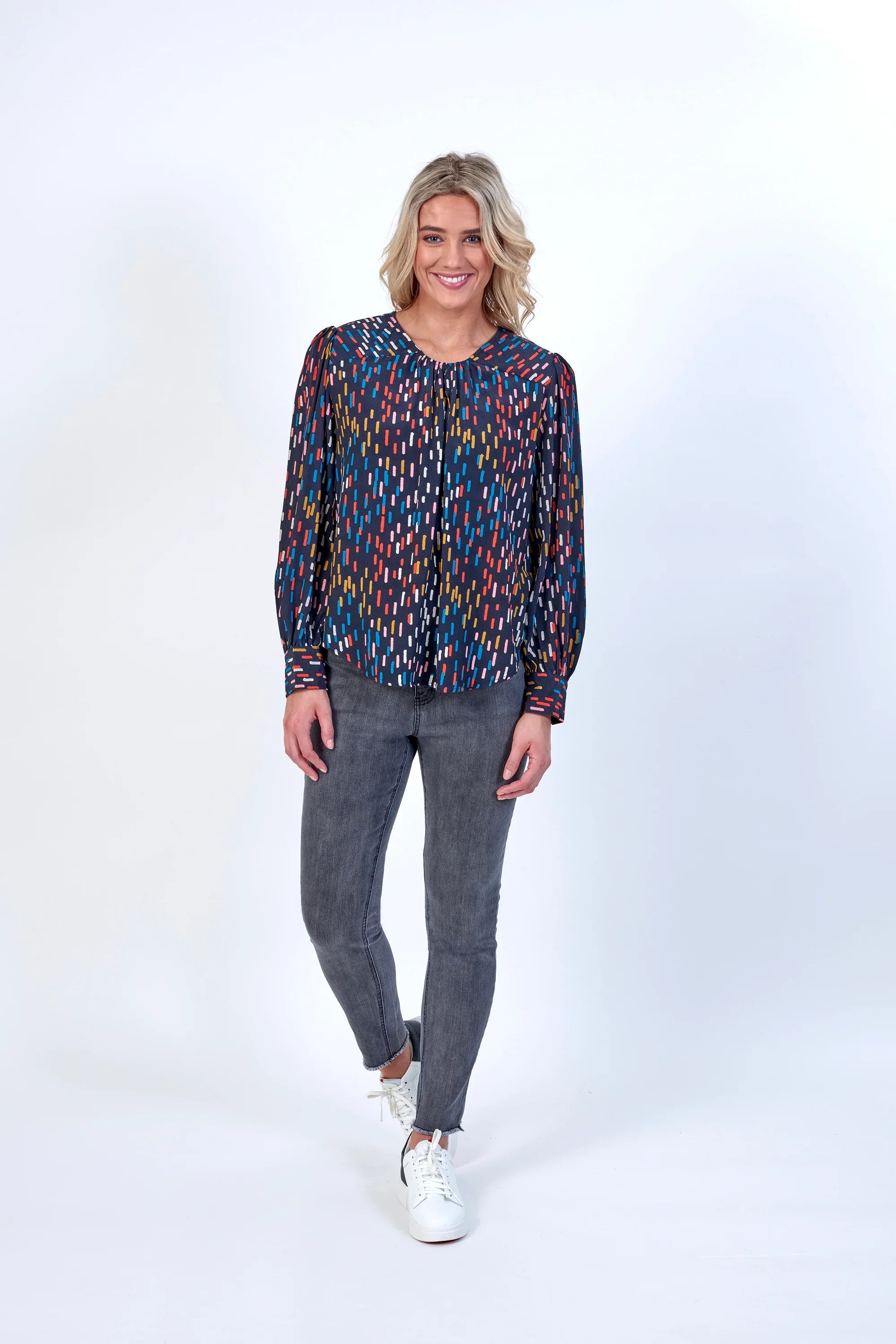 Woman wearing a long sleeve multicolor patterned top with grey skinny jeans and white sneakers