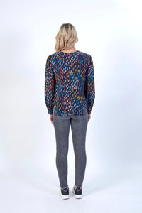 Woman wearing a long sleeve patterned top and grey jeans, seen from the back