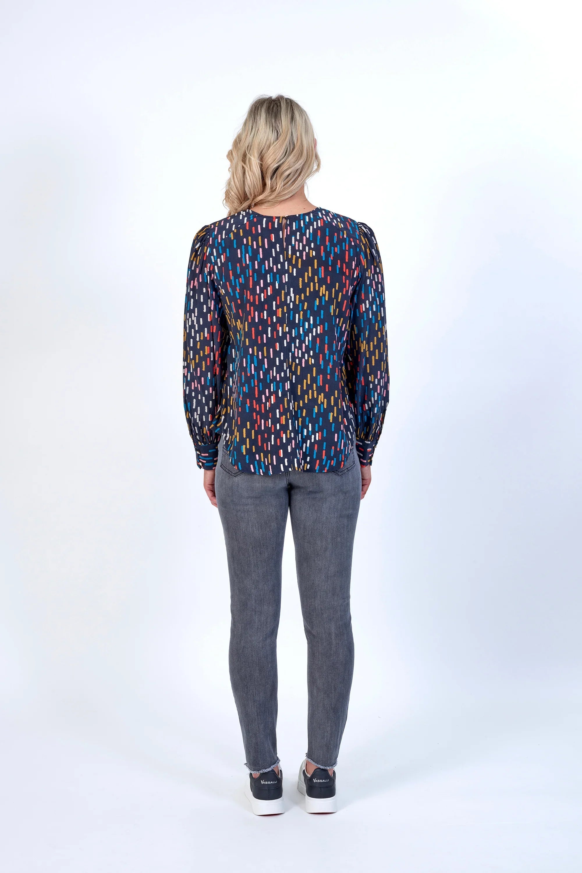 Woman wearing a long sleeve patterned top and grey jeans, seen from the back