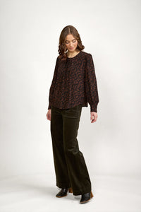 Woman wearing mocha patterned long sleeve blouse with wide leg dark pants and black boots