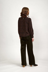 Woman wearing a long sleeve brown abstract print blouse and dark wide-leg trousers