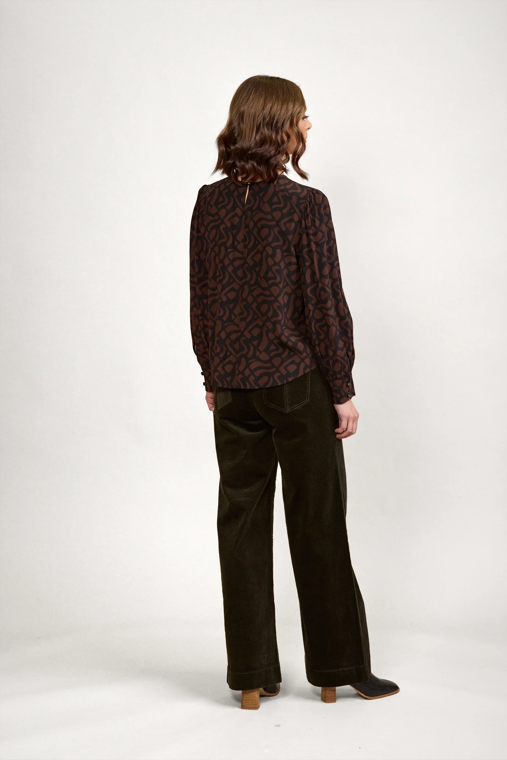 Woman wearing a long sleeve brown abstract print blouse and dark wide-leg trousers