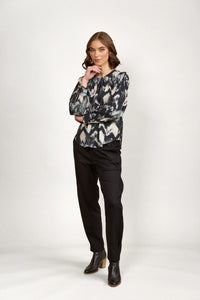 Woman wearing abstract print long sleeve blouse with black pants and ankle boots, studio background
