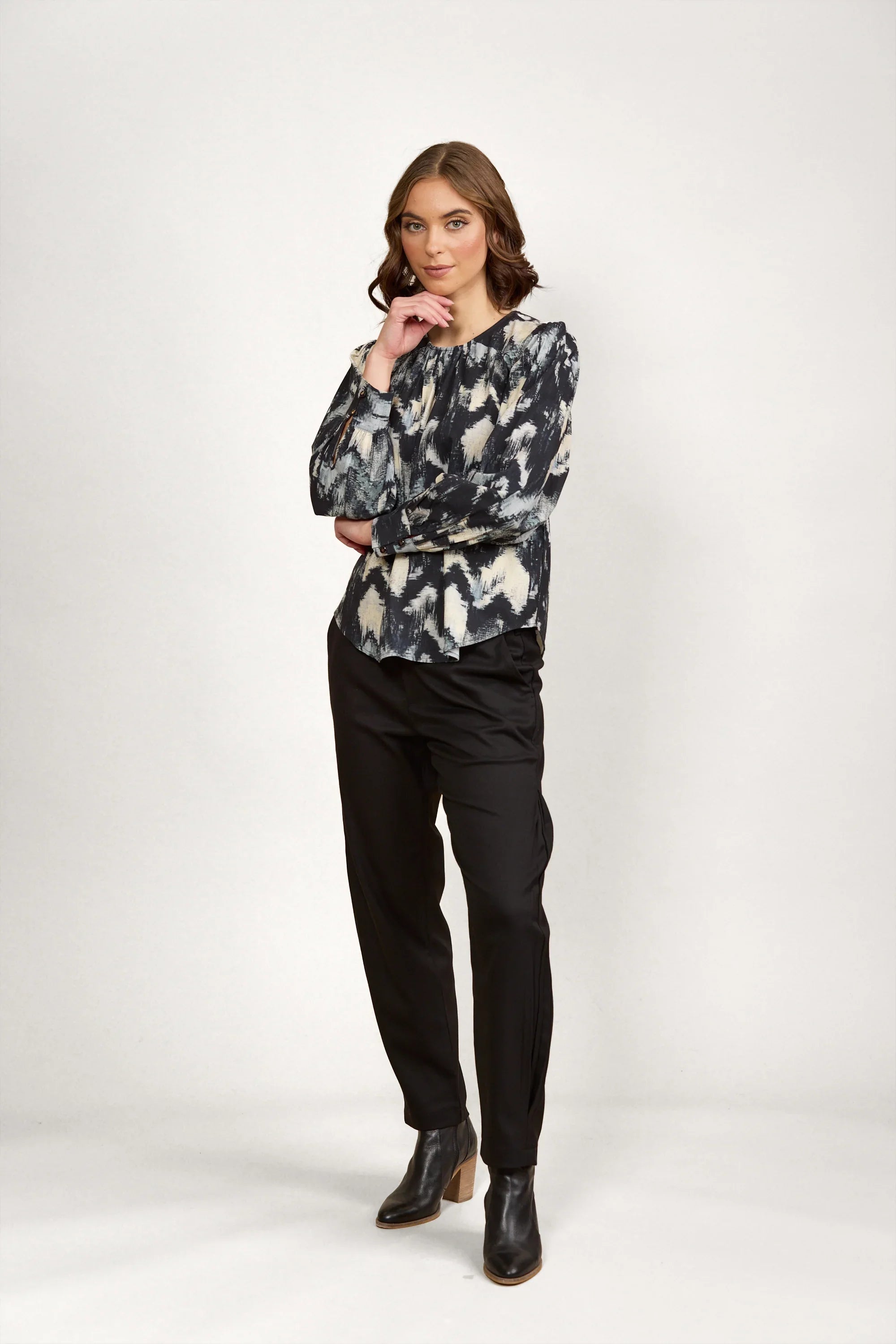 Woman wearing abstract print long sleeve blouse with black pants and ankle boots, studio background