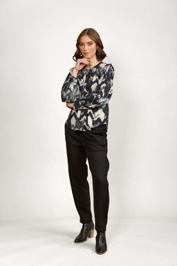 Woman wearing abstract print long sleeve blouse with black pants and ankle boots, studio background