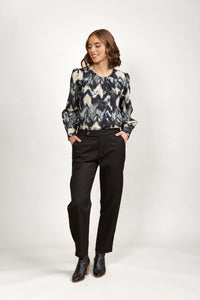 Woman wearing abstract patterned long sleeve blouse with black trousers and ankle boots