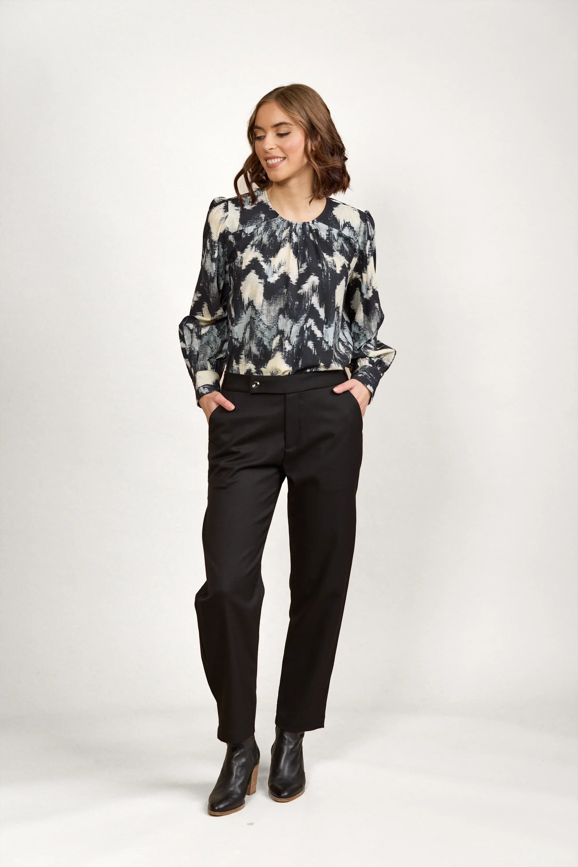 Woman wearing abstract patterned long sleeve blouse with black trousers and ankle boots